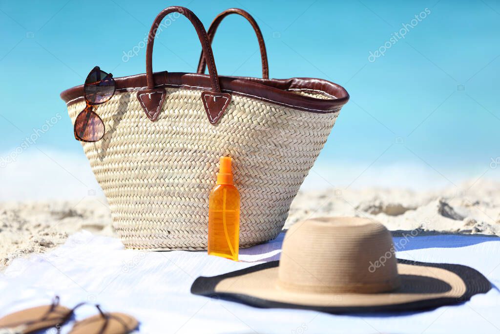 Accesorios de playa esenciales incluyendo protector solar, sombrero y bolsa de playa sobre la arena
